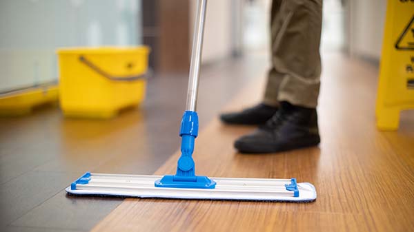 Janitorial services associate cleaning a commercial hard floor with a professional microfiber mop next to a caution wet floor sign